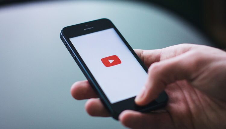 uma pessoa segurando um smartphone que exibe a tela inicial do aplicativo YouTube
